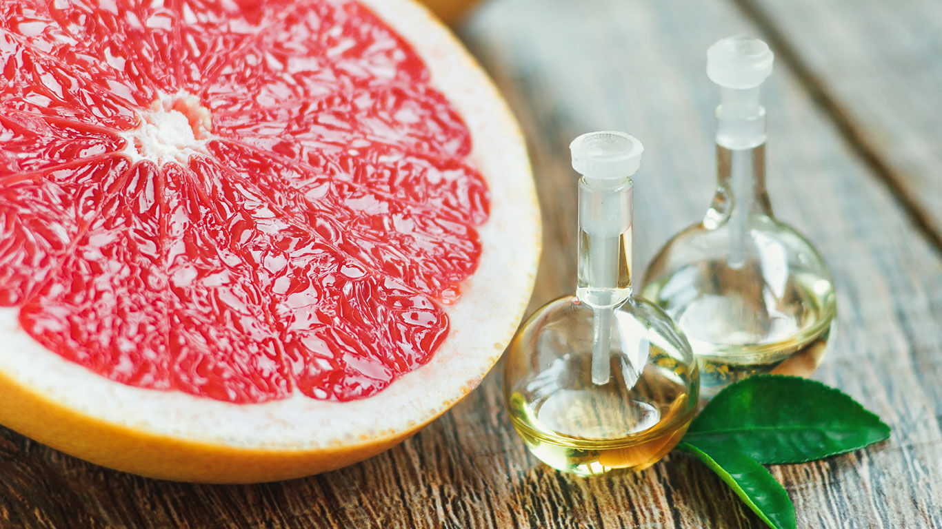 Halbierte Grapefruit neben Fläschchen mit ätherische Öl der Grapefruit
