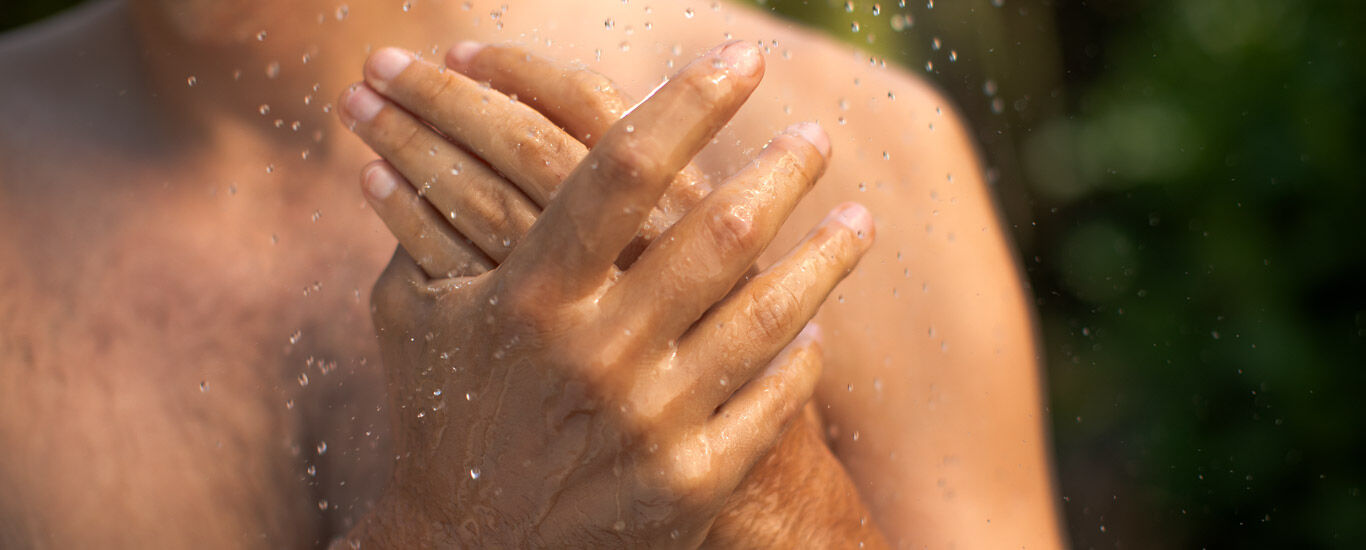 Nahaufnahme zweier Hände eines Mannes unter der Dusche. 