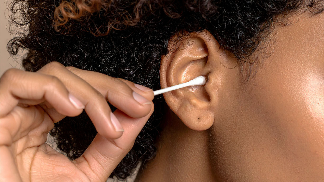 Hand f&uuml;hrt ein Wattest&auml;bchen vorsichtig an das Ohr.