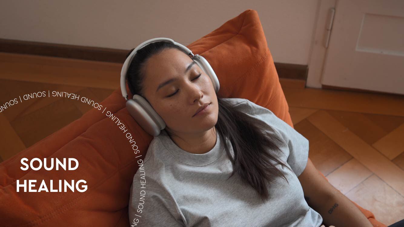 Frau entspannt mit Kopfhörern auf orangenem Sessel. Weißes Textoverlay "Sound Healing", auch in Kreisform um den Haupttext.