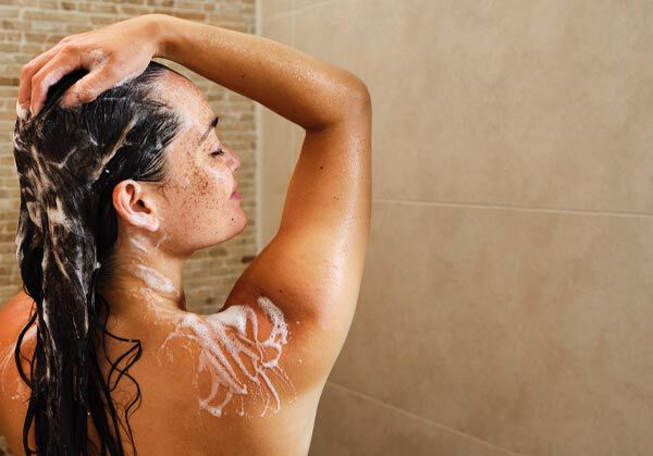 Frau steht unter der Dusche und wäscht ihre Haare.