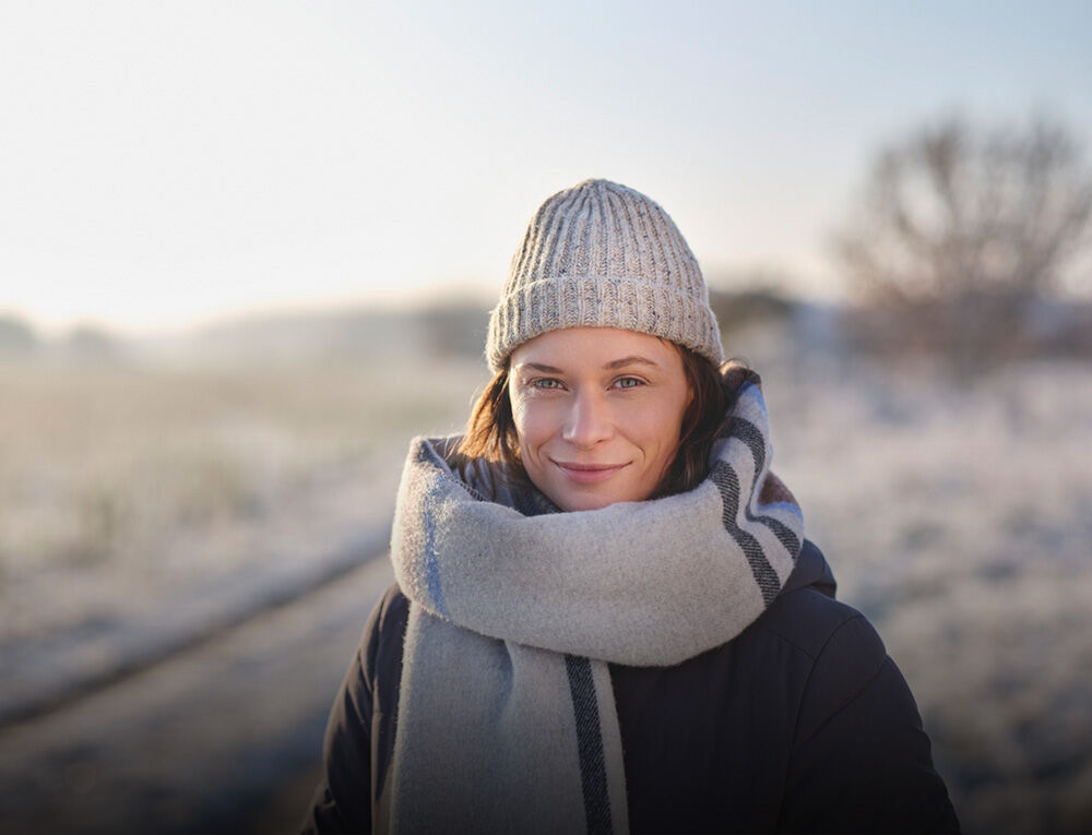 Frau in Winterkleidung steht in verschneiter Landschaft. 
