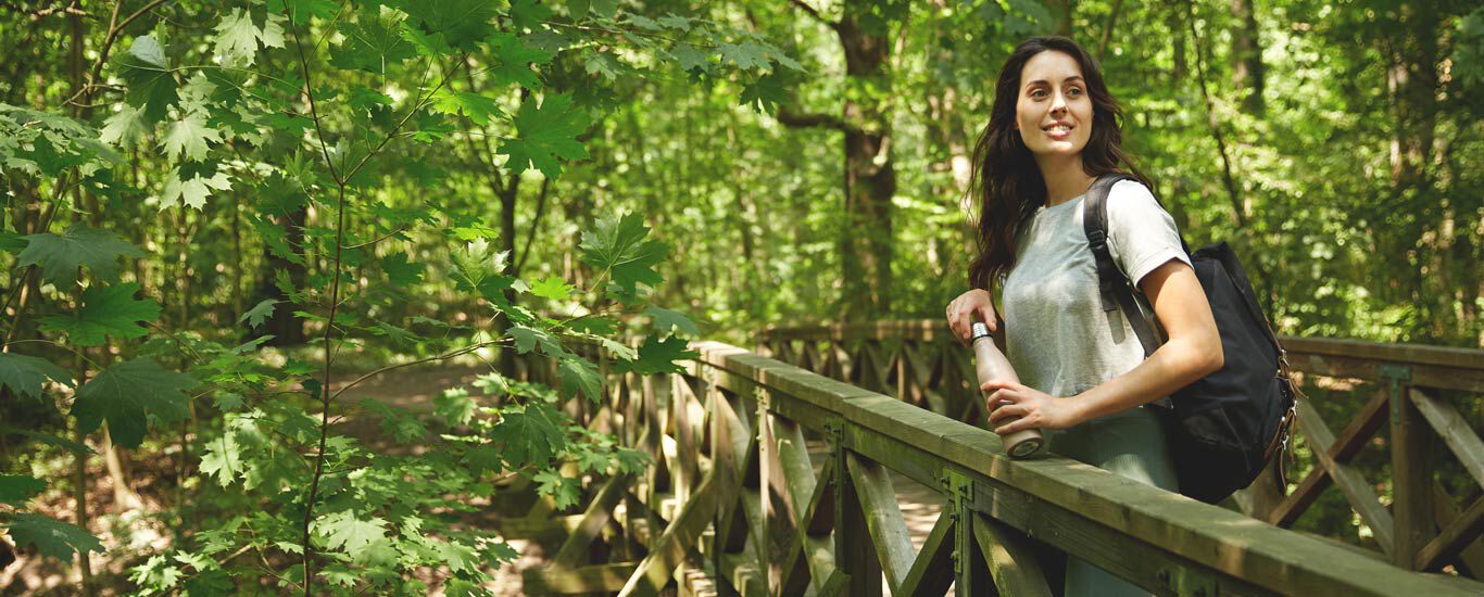 Frau lehnt an einer Holzbrücke im Wald für eine kurze Pause. 