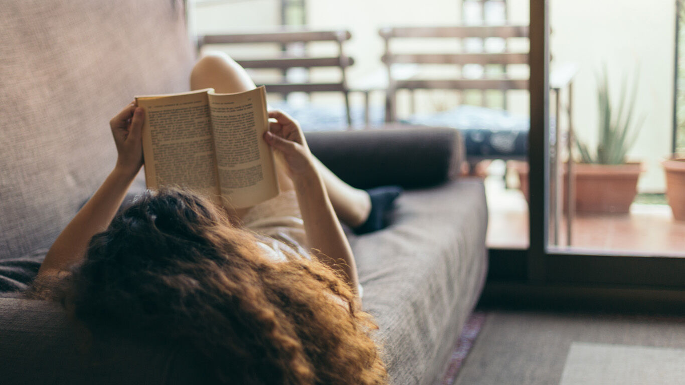 Woman lying on the coach and reading a book.