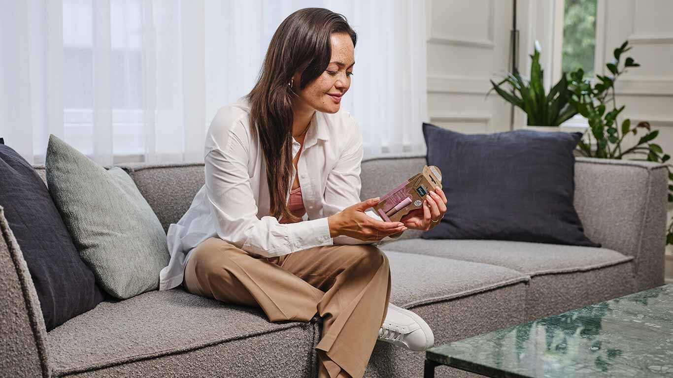 Frau sitzt auf dem Sofa und hält eine Kneipp Lippenpflege-Verpackung mit Silphie-Papier in den Händen.