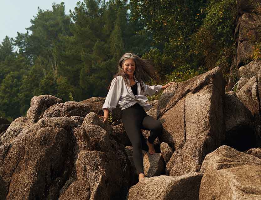 Grauhaarige Frau klettert auf Felsen. 