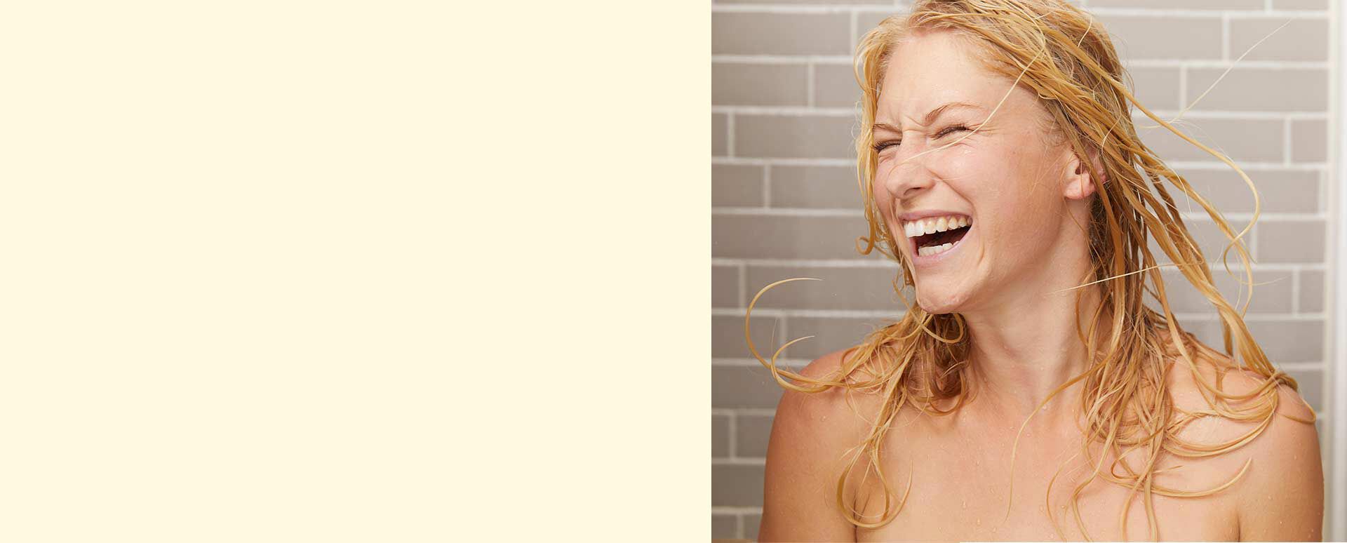 Frau mit blonden nassen Haare steht glücklich unter der Dusche. 