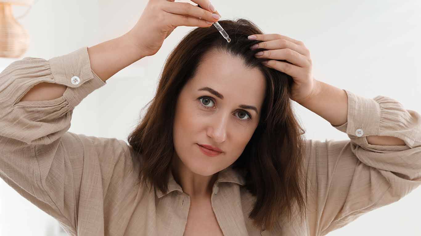 Frau pflegt Kopfhaut mit Pipette. 