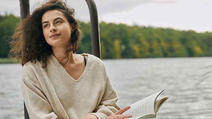 Frau entspannt mit einem Buch am See. 