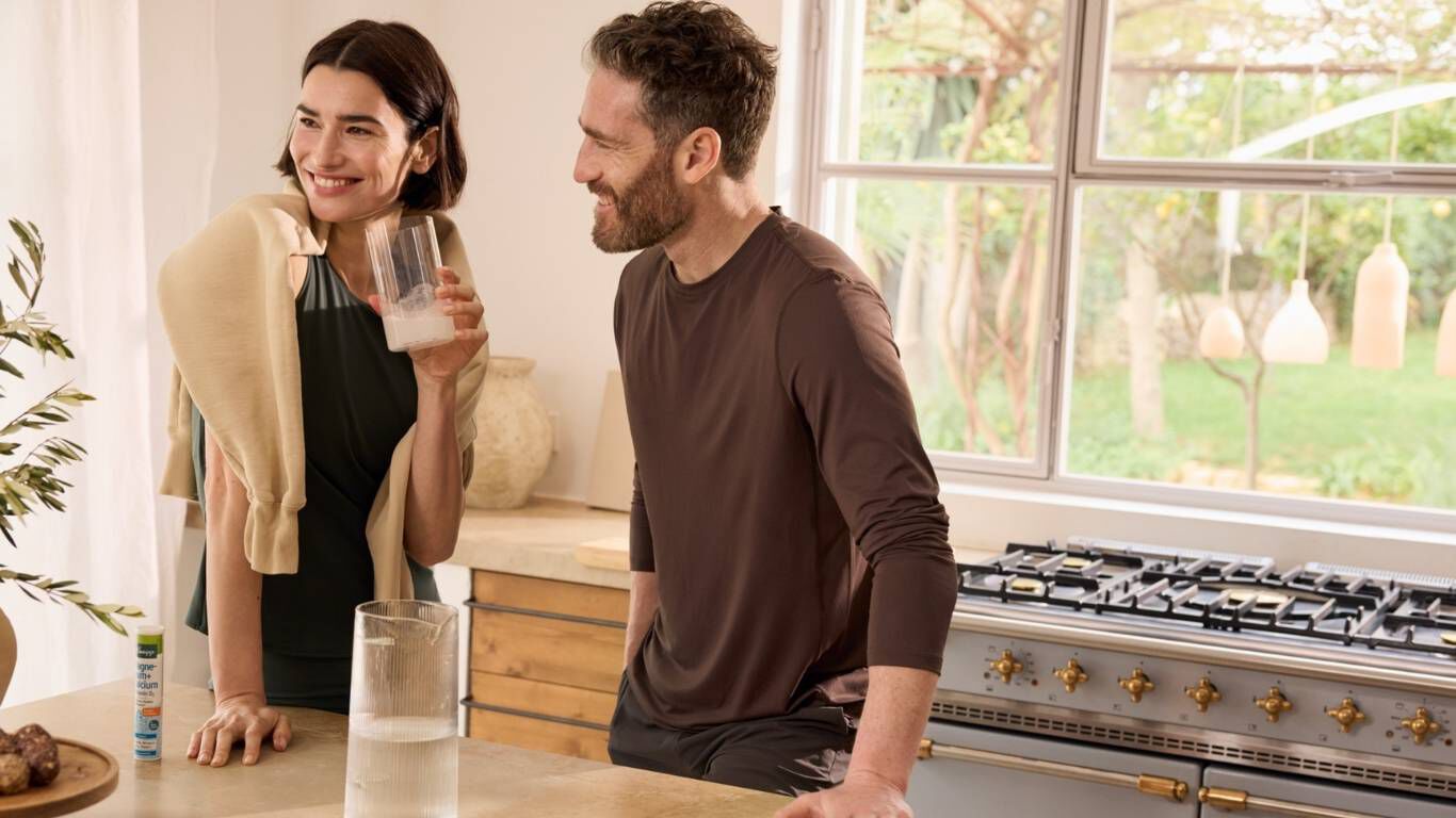 Paar stehen in einer K&uuml;che an einer Arbeitsplatte und trinken aus Gl&auml;sern.