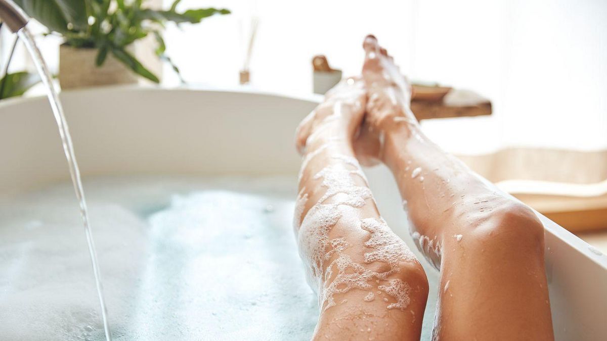 Frau liegt in der Badewanne und legt ihre Beine auf die Kante der Wanne.