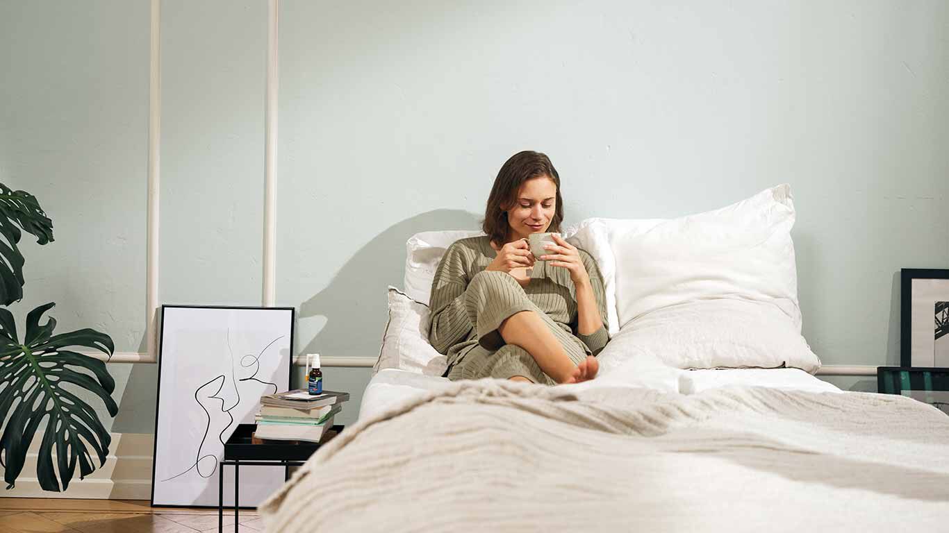 Frau sitzt mit Tasse im Bett.