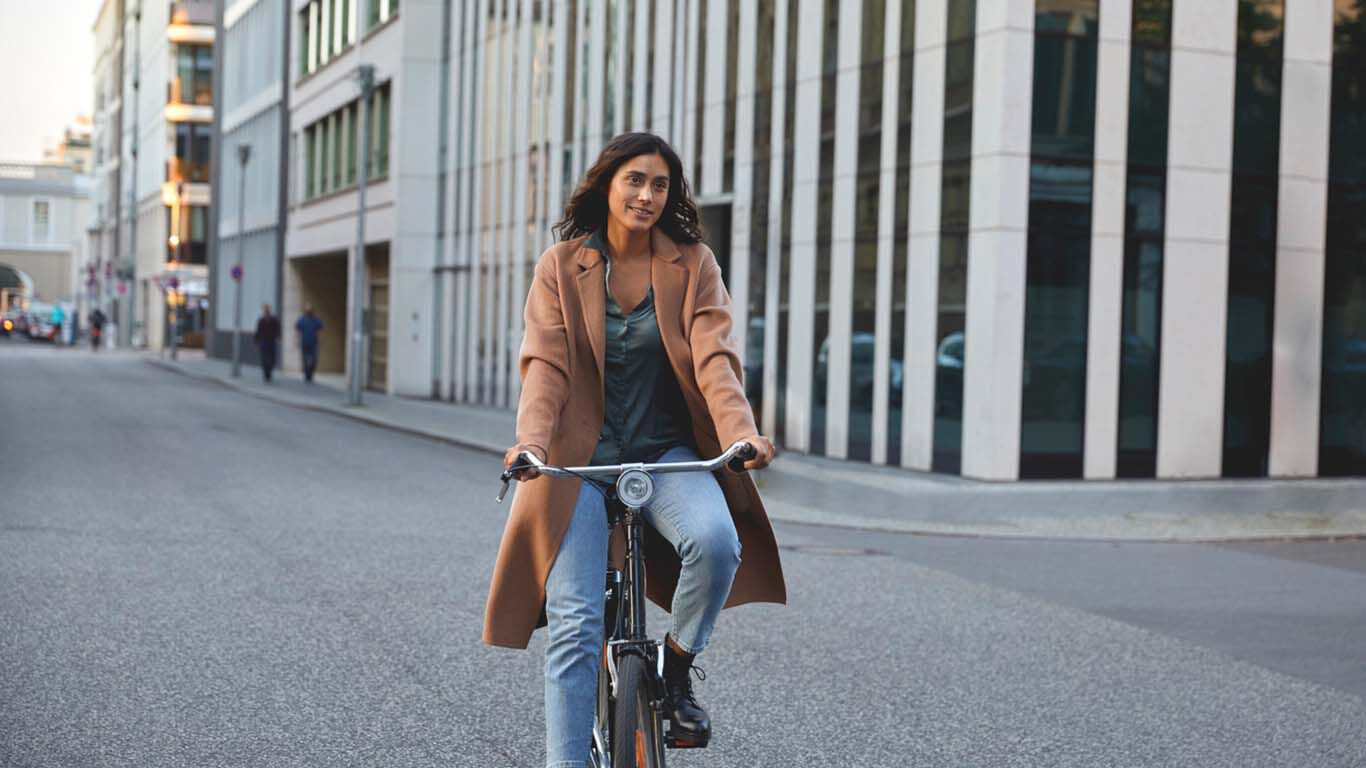 Frau ährt auf einem Fahrrad durch eine moderne Stadtstraße, umgeben von hohen Gebäuden mit Glasfassaden.