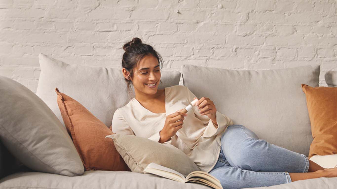 Frau liegt auf einem Sofa mit vielen Kissen und hält einen Lippenpflegestift von Kneipp in der Hand