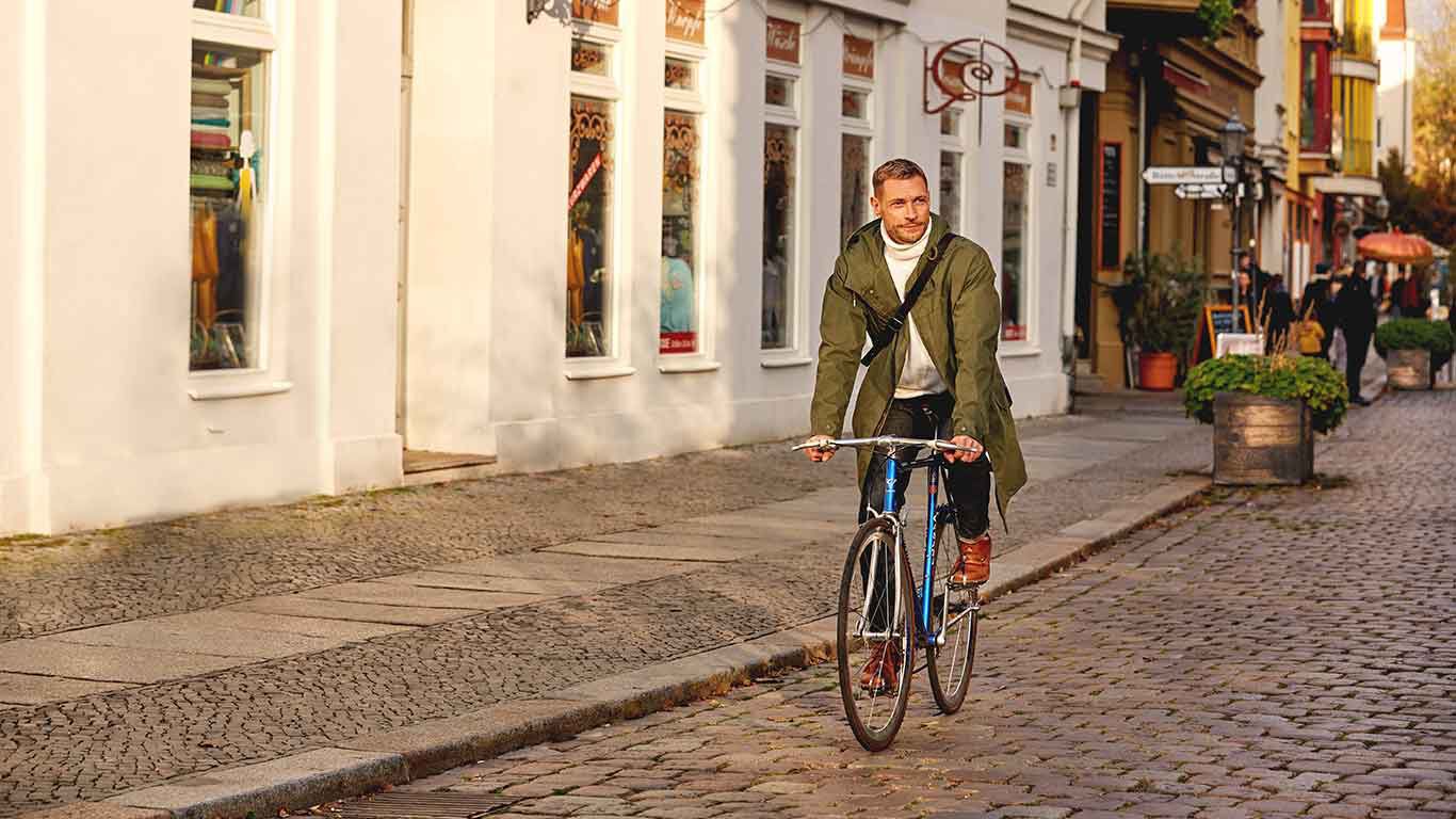 Mann in grünem Parka fährt auf dem Rad durch die Stadt.