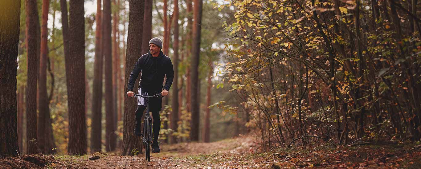 Mann in Sportkleidung fährt auf dem Rad durch den Wald.