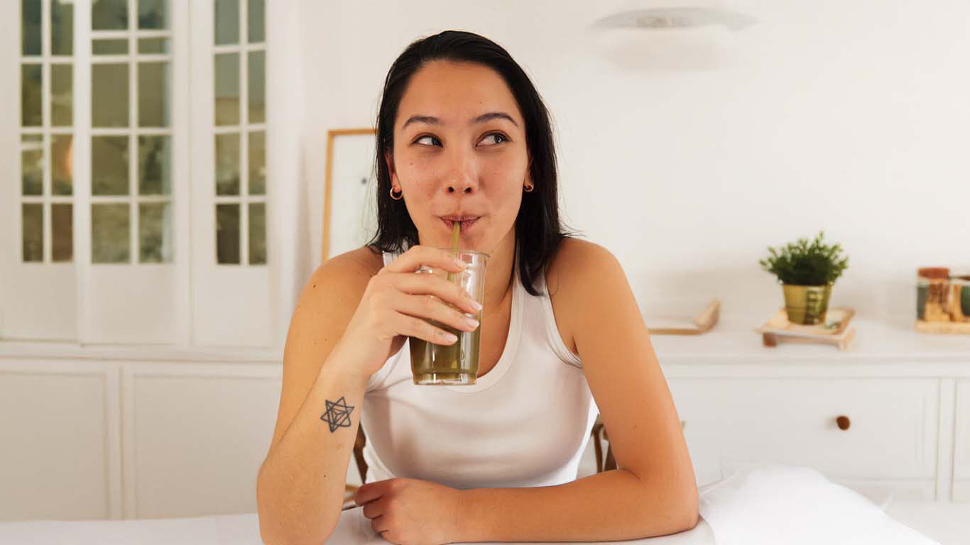 Frau trinkt gr&uuml;nen Smoothie in heller, gem&uuml;tlicher Wohnumgebung.