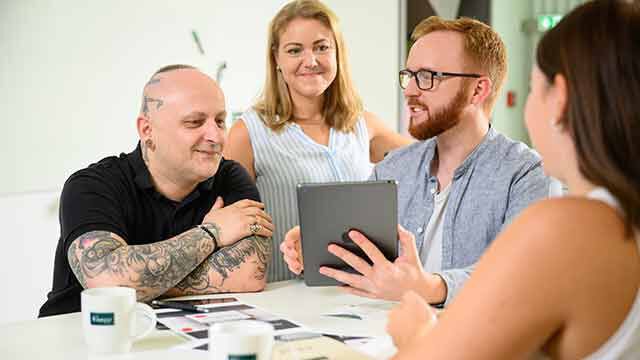 Menschen die um einen Tisch rumstehen mit einem iPad