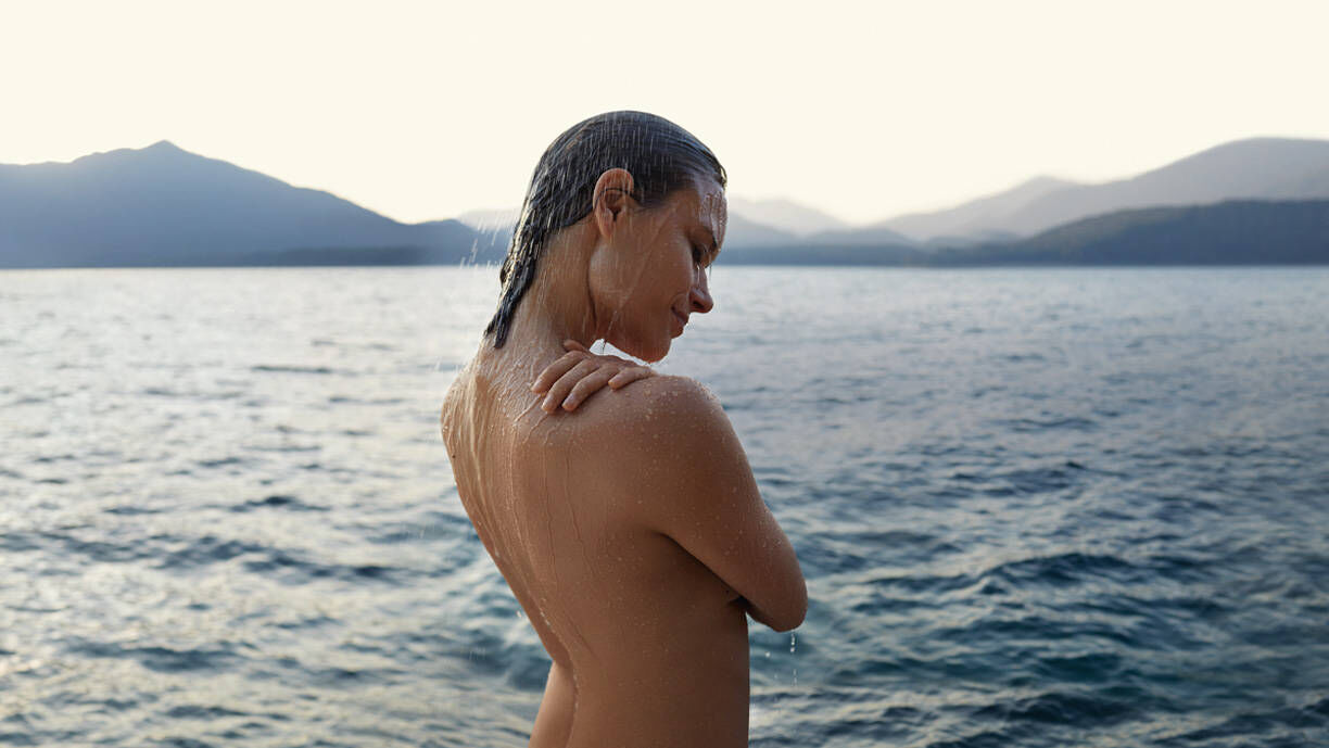 Frau steht nackt vor einem See.