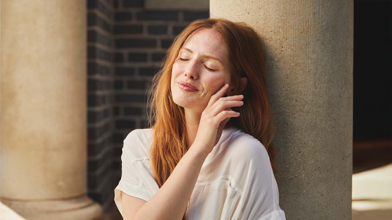 Frau lehnt sitzend an einer Steinsäule und schaut in die Sonne.
