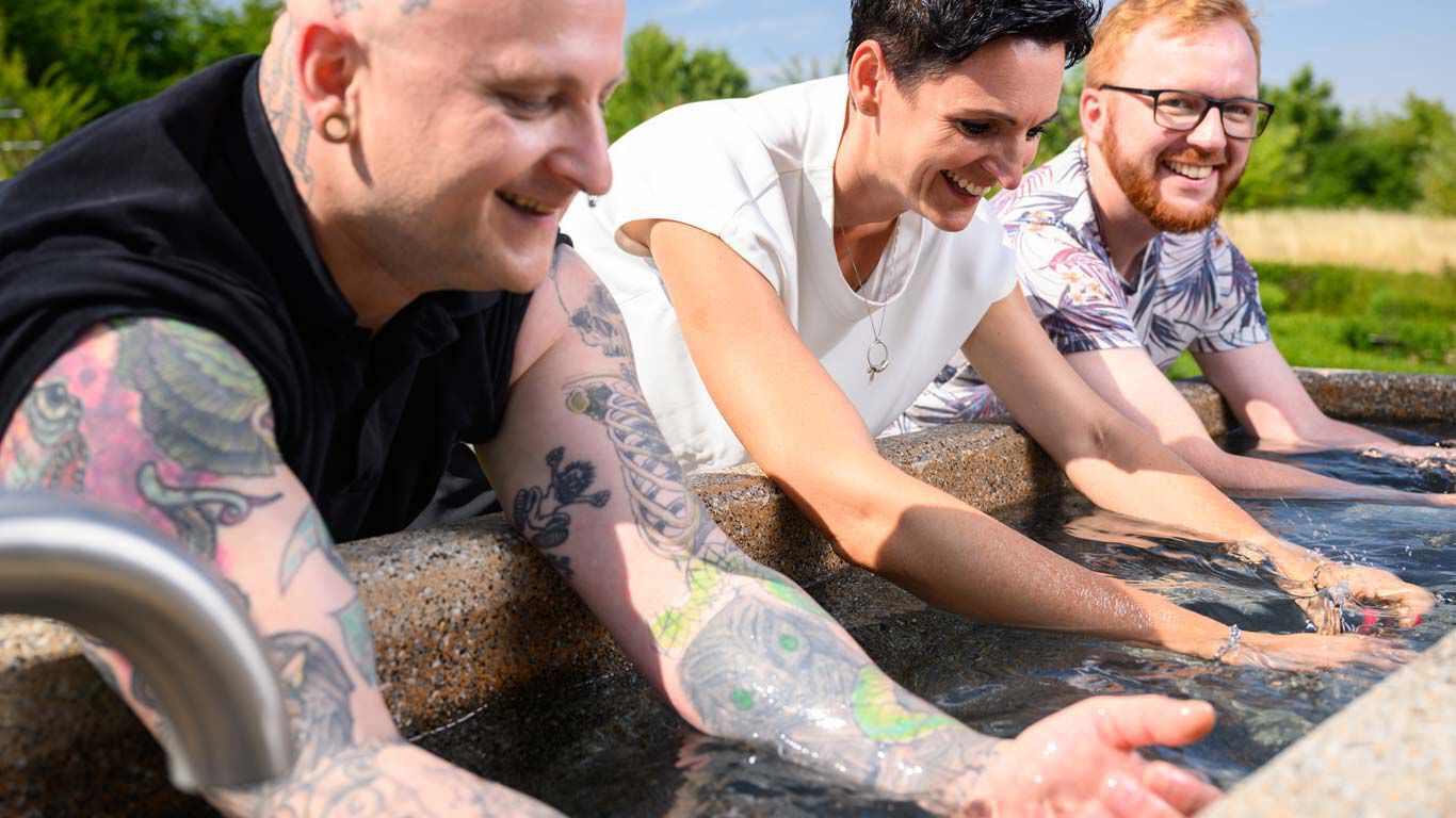 Kneipp Mitarbeitende stehen am Armbad und halten ihre Arme ins k&uuml;hle Wasser