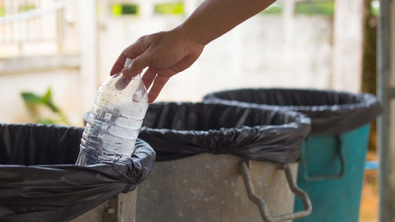 Hand, die Plastikflasche in eine Mülltonne wirft