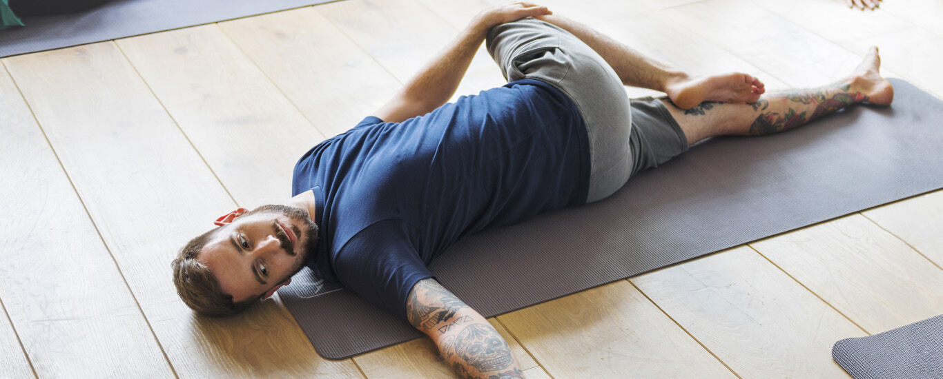 Mann liegt auf einer Yogamatte und führt eine Übung aus.