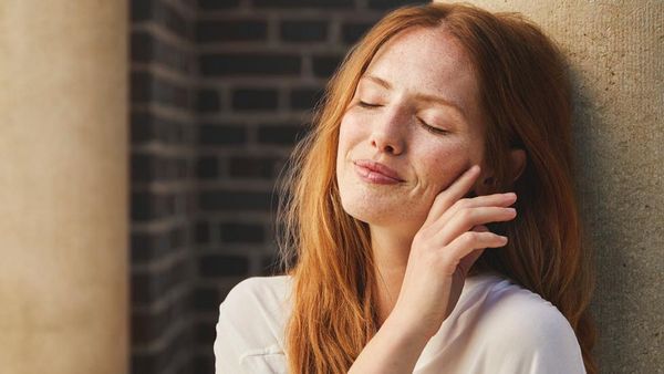 La femme rousse est adossée à un poteau et sourit, satisfaite.