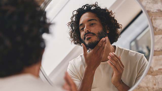 Un homme regarde son visage dans un miroir.