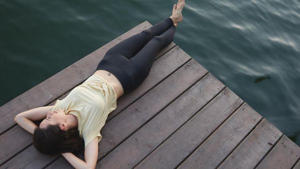 Frau liegt auf einem Steg am See und entspannt.