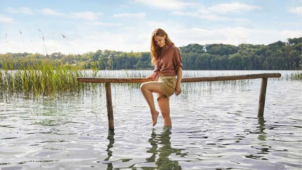 Frau beim Wassertreten in einem See mit hölzernem Handlauf.
