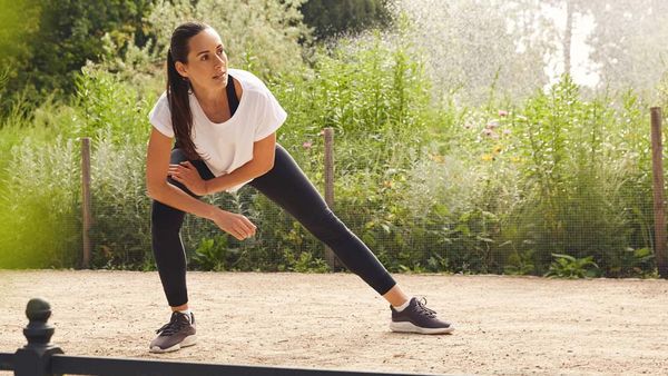 Une femme en tenue de sport étire ses jambes sur un chemin forestier.