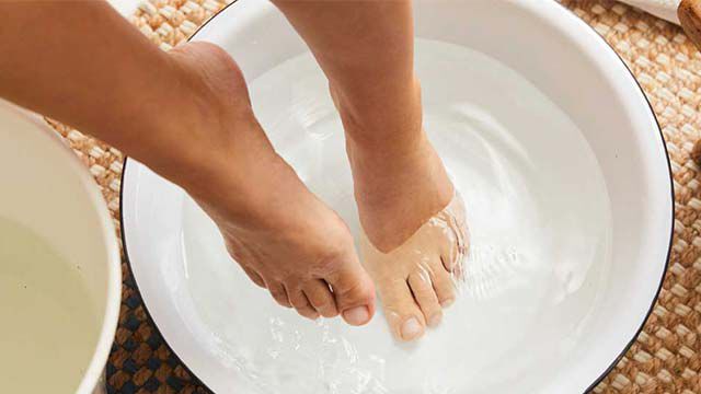 Gros plan sur deux pieds, dont l'un est dans une bassine remplie d'eau. À côté se trouve un seau rempli d'eau.