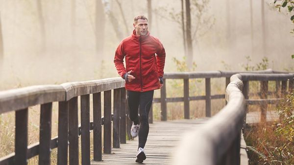 Mann joggt im Morgennebel in roter Jacke über einen Steg.