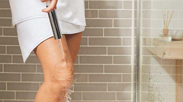 Frau steht in der Dusche und lässt Wasser über ihr Knie laufen, nur die Beine von ihr sind zu sehen.