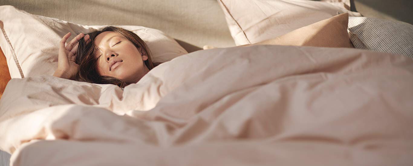 Dunkelhaarige Frau liegt im Bett und schläft.