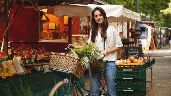 Une femme à vélo se tient sur une place de marché. Dans son panier, elle transporte des légumes.