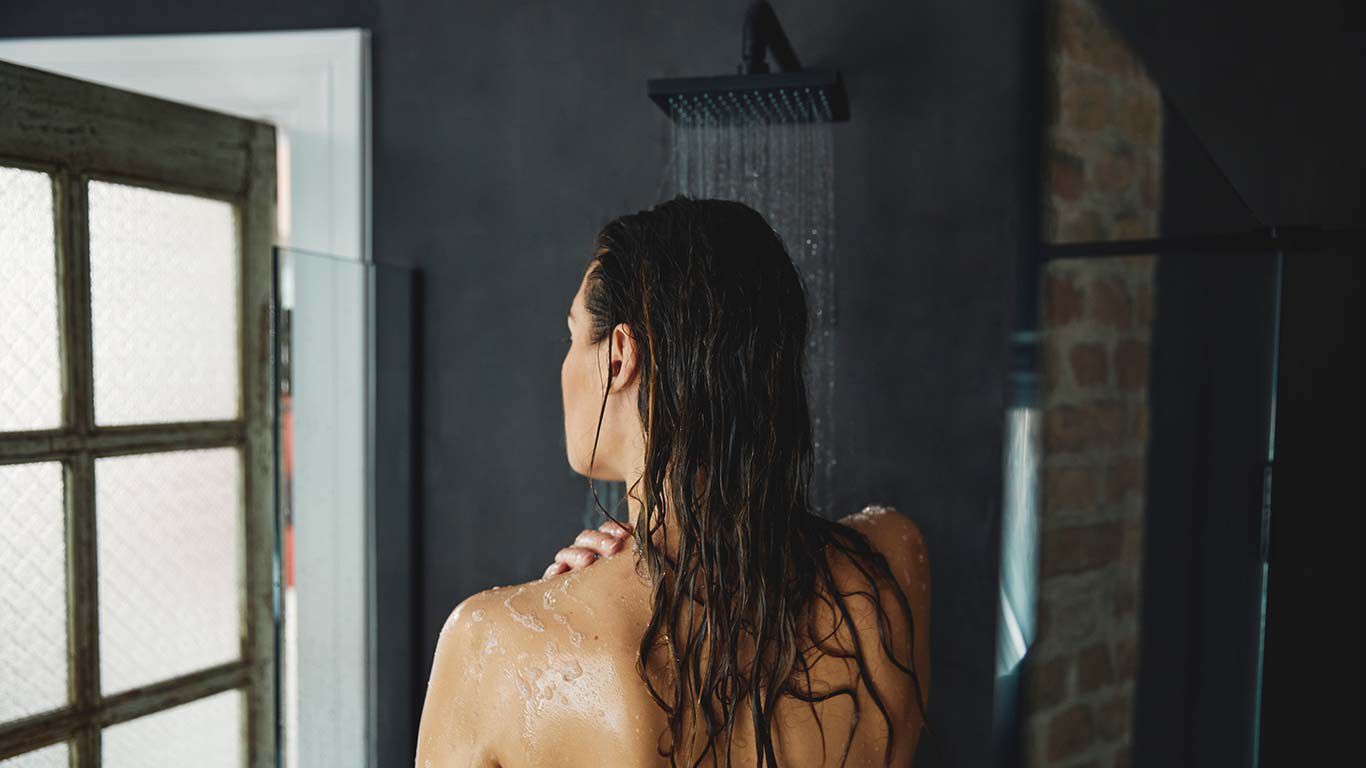 Femme brune aux cheveux mouillés dans la douche. Vue de dos.