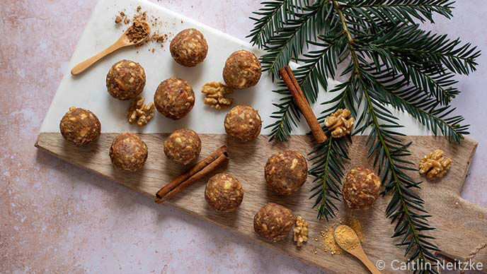 Energy Ball auf Löffel drapiert, daneben Zimtstangen und Sternanis. 