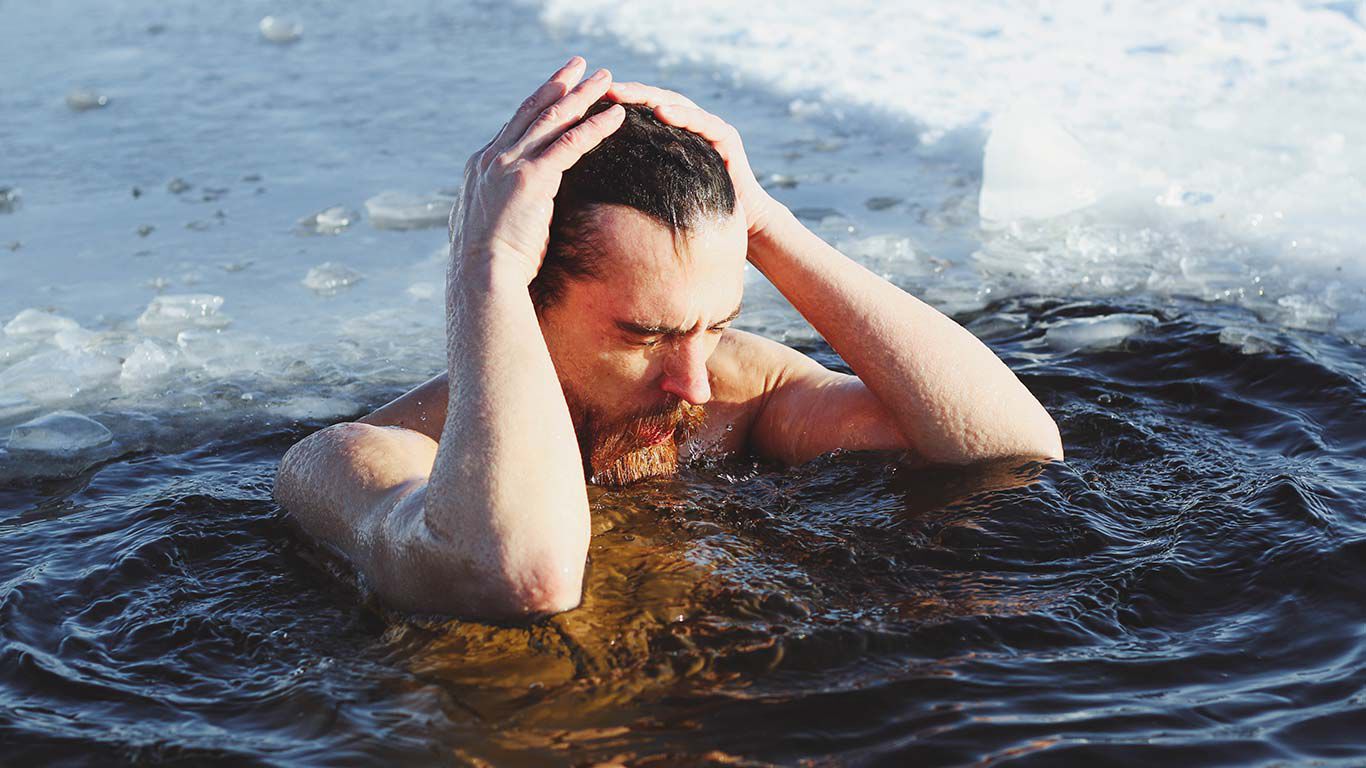 Mann badet brusttief in Eiswasser und streift sich die nassen Haare aus dem Gesicht.