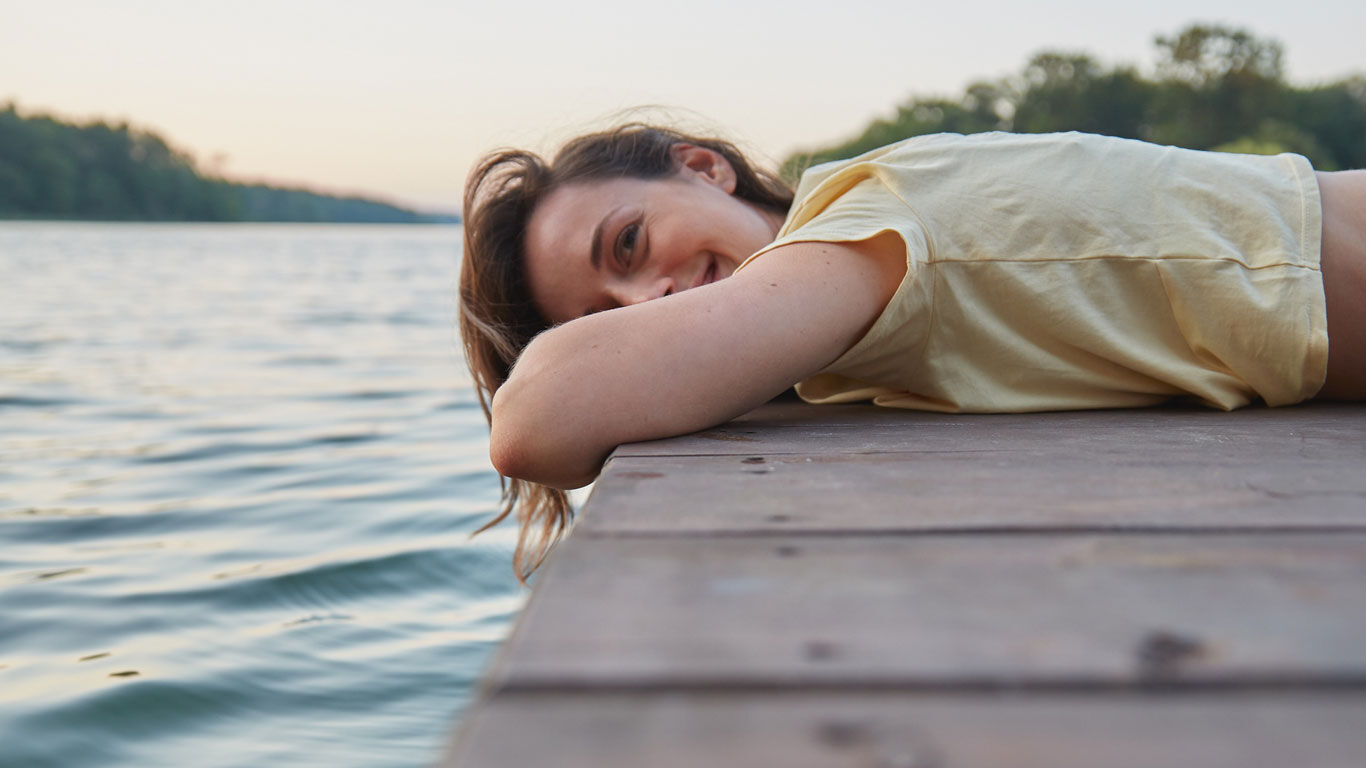 La femme est allongée sur le ventre à gauche sur un ponton et se détend.