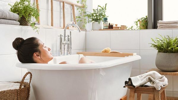Une femme brune avec un chignon se détend dans la baignoire. 
