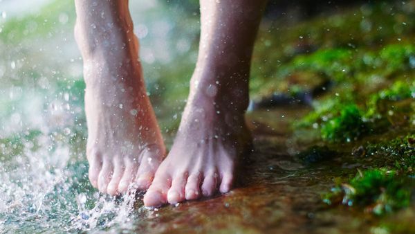 Nahaufnahme von Füßen auf einer moosigen Oberfläche. Wasserspritzer im linken Bildrand.