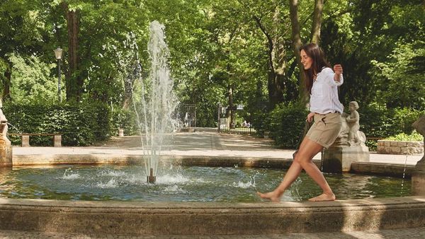 Dunkelhaarige Frau balanciert auf dem Rand eines Springbrunnens. 