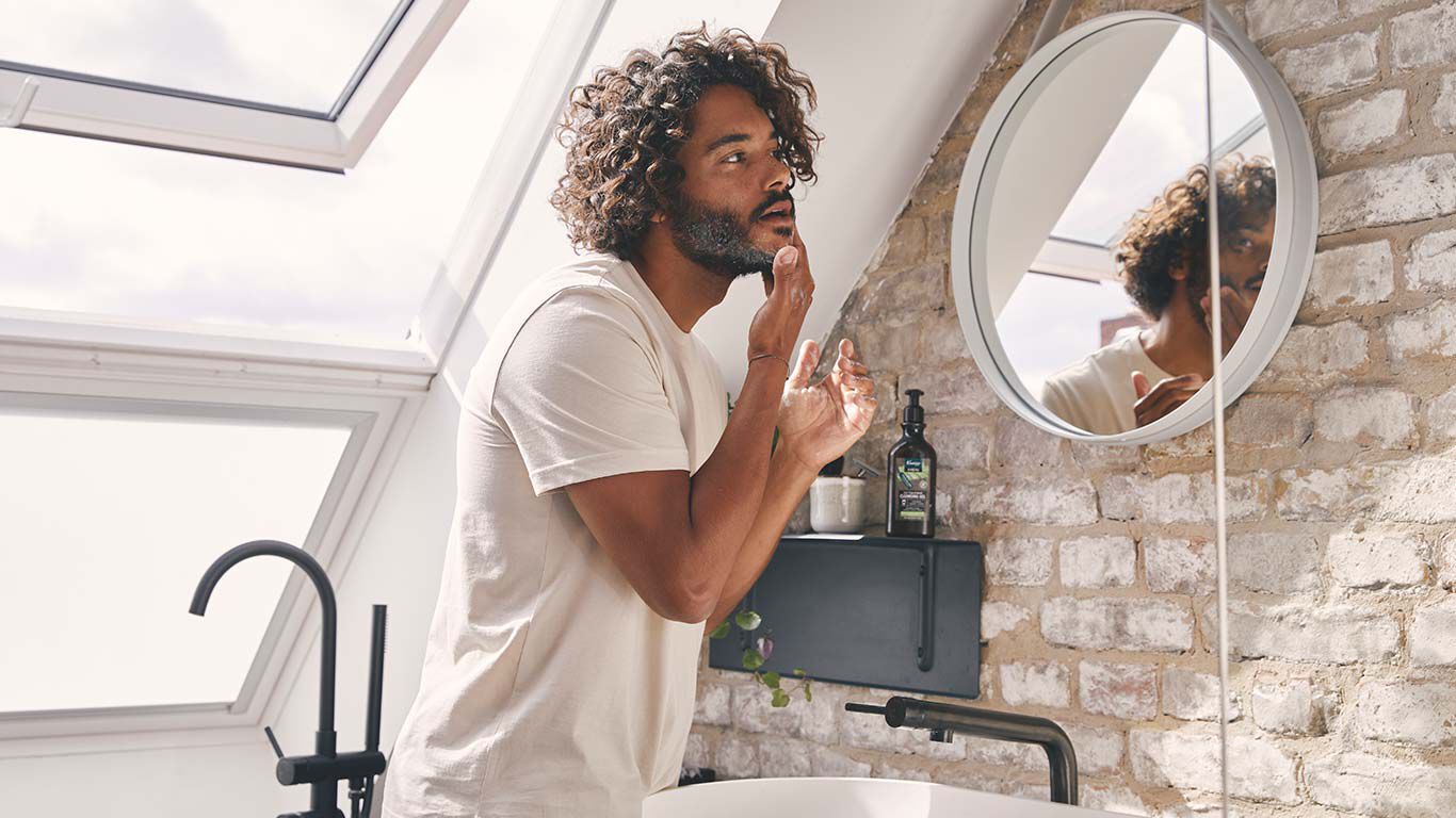 Un homme se tient devant le miroir dans la salle de bain et prend soin de sa barbe.