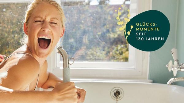 Femme chantant dans une pomme de douche. Signe du jubilé Kneipp avec l'inscription "Moments de bonheur depuis 130 ans".