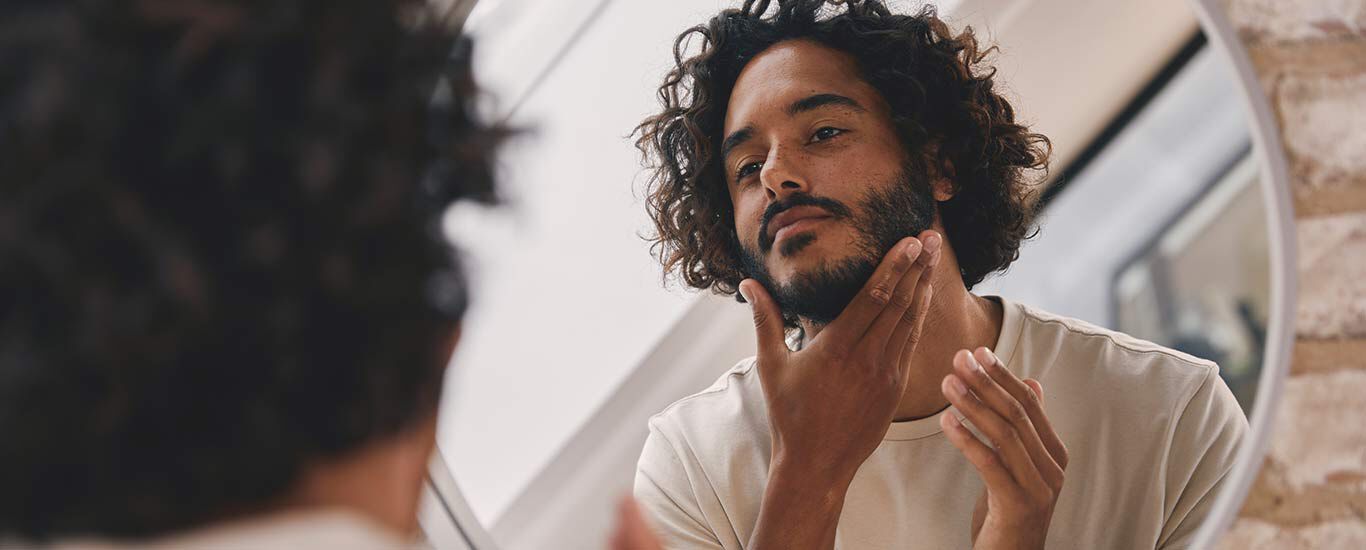 Un homme regarde son visage dans un miroir.