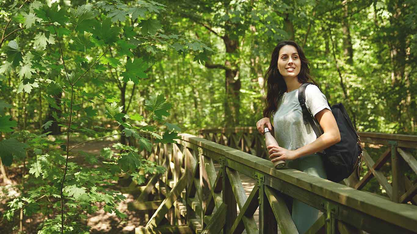 Frau lehnt an einer Brücke und genießt die Natur im Wald. 