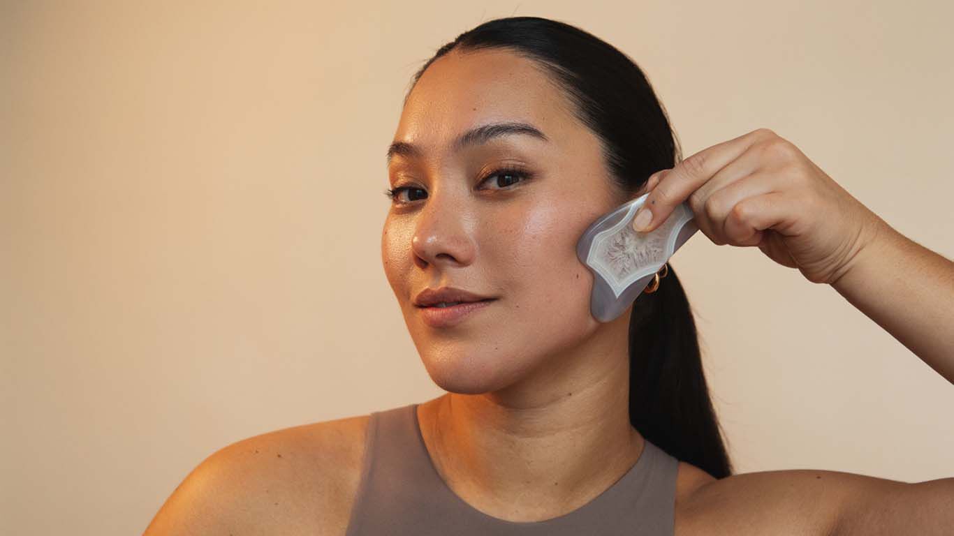 Une femme se masse le visage avec une pierre Gua-Sha le long de la joue.