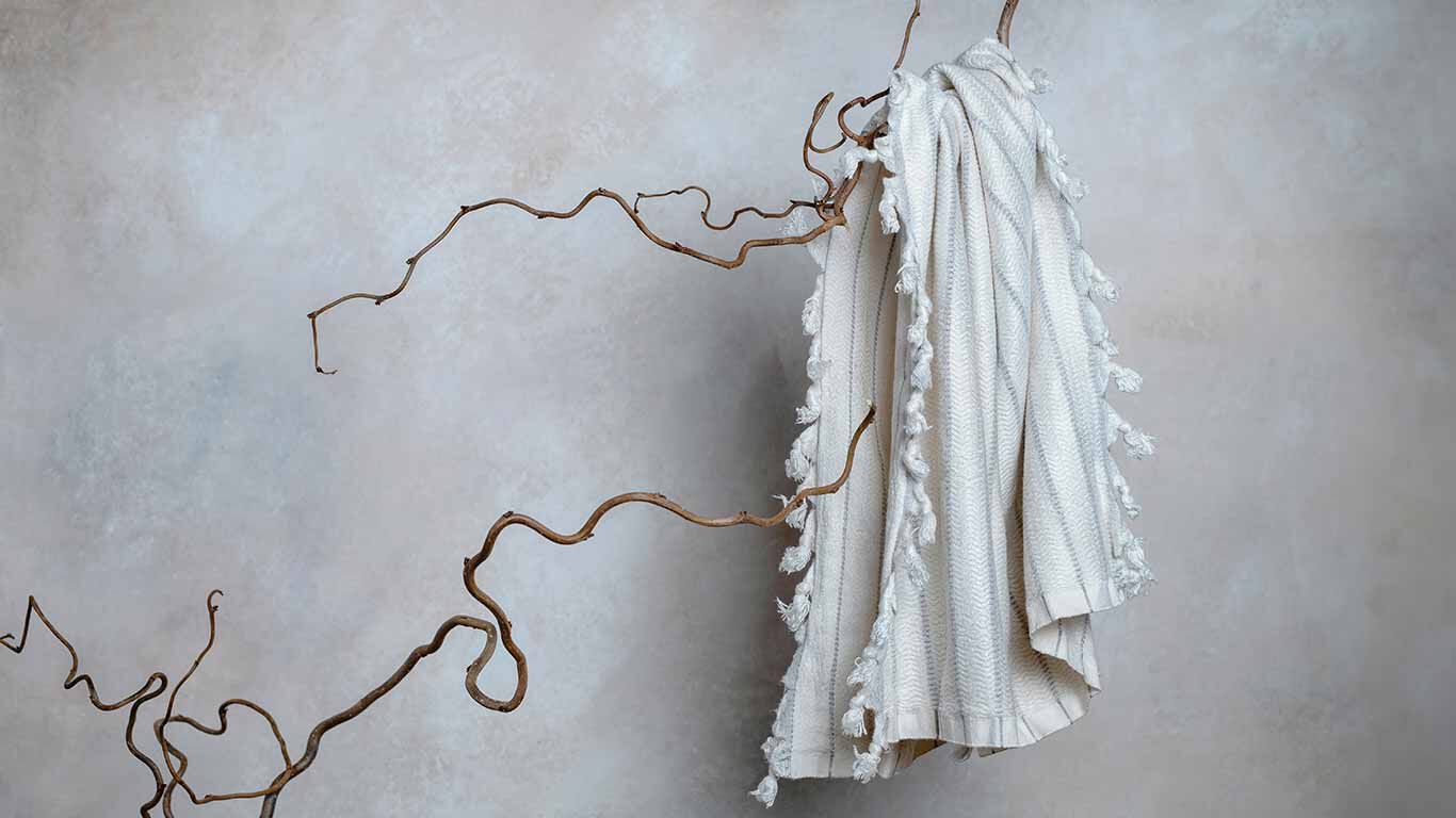 Serviette en lin suspendue au-dessus d'une branche devant un mur en béton. 